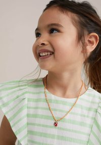 Green and white striped dress with ruffled sleeves, paired with an orange and white beaded necklace featuring a red charm.