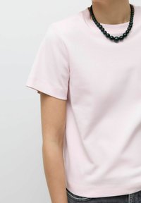 Lichtroze T-shirt met korte mouwen gemaakt van zachte stof, met een ronde hals, gecombineerd met een zwarte kralenketting en goed zichtbare grijze denim jeans.