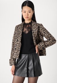 Leopard-print blazer in soft fabric, featuring a notched collar, double-breasted buttons, and three-quarter sleeves, paired with a black top and pleated leather shorts.