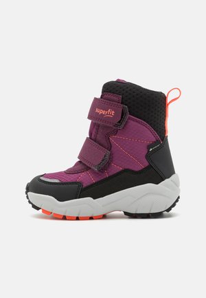 Kinderschuh aus lila und schwarzem Material für den Winter mit doppelten Klettverschlüssen, orangefarbener Schlaufe und robustem weißen und orangefarbenen Sohlen, seitlich dargestellt.