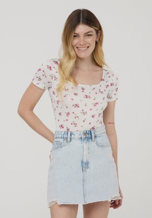 Body a maniche corte con stampa floreale bianca e rose rosa, abbinato a una mini gonna di jeans azzurro chiaro con orlo sfilacciato e dettagli consumati.