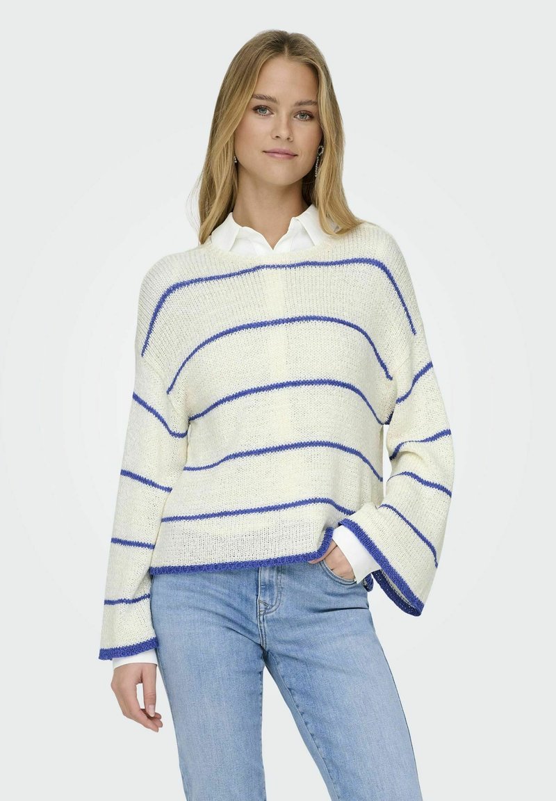 Cremfarbener gestrickter Pullover mit blauen Streifen, lockerer Passform, ausgestellt manche und einer strukturierten Oberfläche, kombiniert mit hellblauen Jeans.