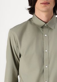 Light green button-up shirt with a collared neckline, featuring textured fabric, rounded edges, and clear buttons along the front.