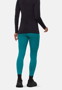 Leggings turchesi con una texture liscia, caratterizzati da un design a cucitura e abbinati a un top nero a maniche lunghe e calzature scure.