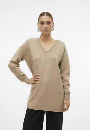 Beige V-Ausschnitt Pullover mit langen Ärmeln, lockerer Passform, weicher Textur und gerippten Bündchen, kombiniert mit schwarzen weit geschnittenen Hosen.