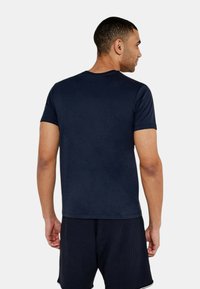 Mörkblå kortärmad t-shirt med rund halsringning, figursydd design och slät textur, bärs tillsammans med texturerade svarta träningsshorts.