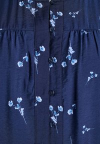 Mornarsko modra obleka s gumbi in belim cvetličnim vzorcem, ki se ponaša z nabranim pasom, zaobljenim izrezom in majhnimi črnimi gumbi spredaj.