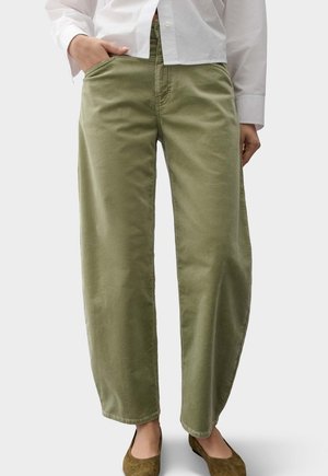 Persoon die licht olijfgroene wijde broek met zijzakken draagt, gecombineerd met bruine platte schoenen en een wit overhemd met knopen.