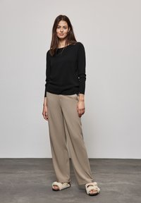 Zwarte long sleeve shirt, beige wijde broek en fuzzy sandalen. Zachte textuur, relaxte pasvorm en neutraal kleurenpalet.