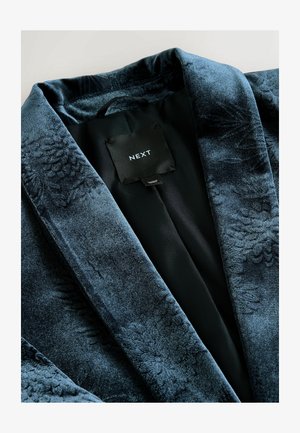 Samtrobe in tiefem Blau mit einem strukturierten Muster und satinierter Innenseite. Das Etikett trägt "NEXT." Klassischer Kragen und offenes Vorderdesign.