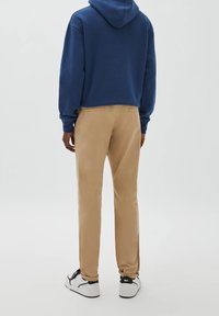 Marineblauer Kapuzenpullover mit Kordelzug und beige Chinos. Die Chinos haben einen geraden Beinverlauf und zwei Gesäßtaschen. Das Schuhwerk ist weiß mit schwarzen Akzenten.