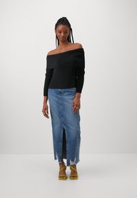 Schwarzes, geripptes Off-Shoulder-Top, kombiniert mit einem langen Jeansrock mit Schlitz vorne und ausgefranstem Saum; das Model trägt gelbe Sandalen mit Riemchen.