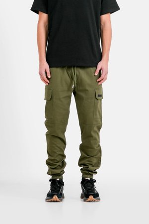 Olijfgroene cargo-broeken, met twee voorzakken, elastische manchetten en een tailleband met trekkoord. Gecombineerd met zwarte sneakers.