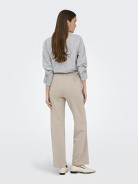 Chemise à rayures à manches retroussées, pantalon large beige et chaussures slip-on de couleur claire, vues de dos.