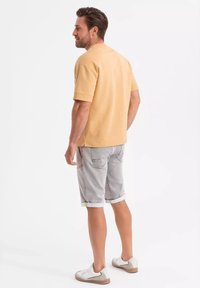 Camiseta de manga corta beige, pantalones cortos de mezclilla grises con dobladillo enrollado y zapatillas blancas. Diseño simple, corte casual, sin patrones ni logos visibles.