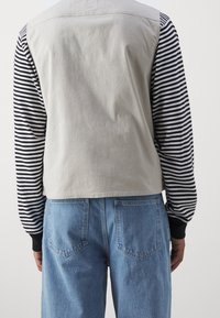 Tessuto grigio sopra con maniche a righe bianche e nere, abbinato a jeans di denim azzurro chiaro con tasche posteriori.