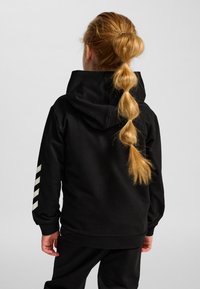 Sudadera con capucha negra con una gran capucha, puños acanalados y un dobladillo recto. Presenta rayas diagonales blancas en la manga izquierda. Textura de tela suave.