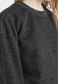 Sudadera negra con textura, de cuello redondo y mangas largas, con un sutil efecto brillante en toda la tela.