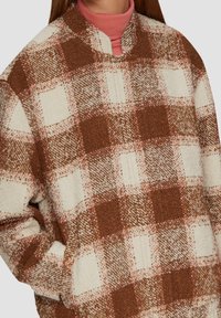 Brown and cream checkered flannel jacket with a soft texture, featuring a collarless design and side pockets.
