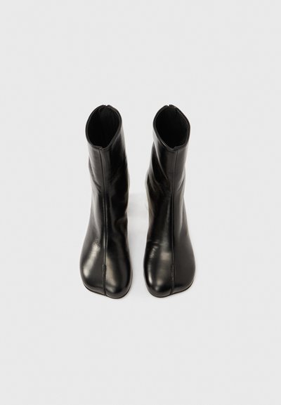 Černé kožené kotníkové boty s elegantním zužujícím se designem, bočními zipy a hladkou strukturou, s špičatou špičkou a minimálním zdobením.
