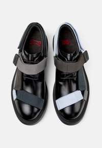 Zapatillas negras con tiras elásticas en gris y azul claro, acabado de cuero suave y logotipos rojos en contraste en las plantillas.