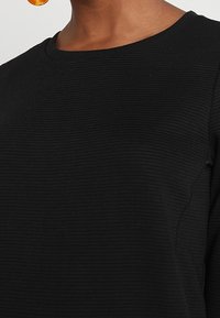 Maglione nero a coste con scollatura rotonda e texture liscia. Inquadratura ravvicinata dei dettagli del tessuto e della cucitura.