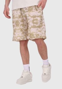 Beige camouflageshorts med en tekstureret overflade, der har en afslappet pasform og sidelommer. Sammen med hvide sneakers og sokker.