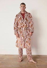 Accappatoio a righe rosse e bianche con motivo dell'omino di pan di zenzero, abbinato a pantaloni coordinati. Il tessuto sembra morbido, con una vita regolabile.