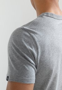 Harmaa lyhythihainen t-paita, joka on valmistettu pehmeästä kankaasta. Paidassa on pyöreä kaula-aukko ja pieni logotagi vasemmassa hihassa.