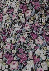 Närbild av tyg med tät blommönster som har rosa, vita, gula och blå blommor på en svart bakgrund med samlad sömnad.