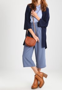 Granatowe długie kimono, jasnobłękitna koszula z kołnierzykiem, luźne niebieskie culottes, beżowe skórzane botki za kostkę oraz brązowa skórzana torba na ramię.