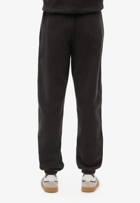 Pantalones deportivos de algodón negros con puños elásticos, un ajuste relajado y una textura suave; combinados con zapatillas blancas con suelas marrones.