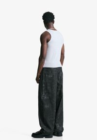 Gray tank top, loose-fitting black pants with a faded texture, and black shoes. The model is viewed from the back against a white background.