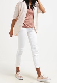 Pletený kardigan v jemně růžové barvě, s krátkým rukávem; upnutá béžová košile; bílé úzké džíny; jemně růžové tenisky se šněrováním a perforovanými detaily.