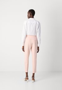 Camicia bianca a maniche lunghe, pantaloni rosa su misura con vestibilità slim e tasca posteriore, abbinati a scarpe beige con tacco. Design semplice e moderno.