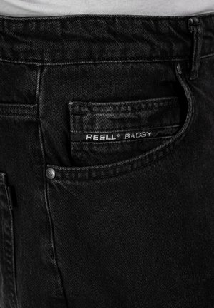 Schwarze baggy Jeans aus Denim, mit einer Gesäßtasche, die ein sichtbares Etikett "REELL BAGGY" und einen Metallknopf bringt.