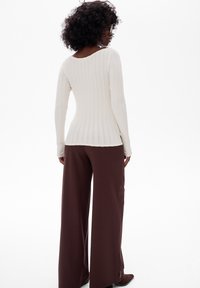 Biały, prążkowany top z długim rękawem zestawiony z szerokimi brązowymi spodniami. Top ma okrągły dekolt i fakturowany materiał. Spodnie są luźne.