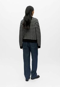 Melnbalts rakstots adīts džemperis ar apaļo kakla izgriezumu, ribotām piedurknēm un apakšmalu, kombinēts ar tumši zila platā stila džinsiem.