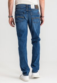 Niebieskie męskie jeansy z denimu o dopasowanym kroju, pięcioma kieszeniami, kontrastującym szwem oraz brązową skórzaną naszywką na pasie.