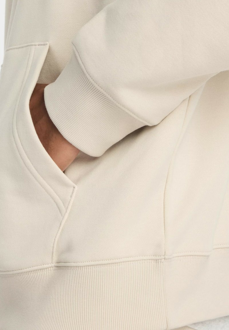 Beige Sweatshirt mit einer Kängurutasche, gerippten Bündchen und einer glatten Textur. Der Stoff hat einen subtilen Glanz und ein lässiges Passform-Design.