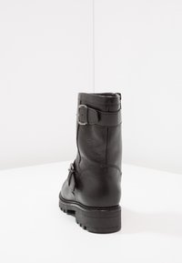 Bota de cuero negro hasta el tobillo con un acabado texturizado, cierre con cremallera lateral y una hebilla decorativa en el lado exterior, con una suela resistente y con relieve.