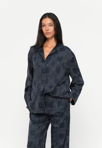 Set di abbigliamento da casa blu navy composto da una camicia button-up a vestibilità ampia e pantaloni coordinati, con un motivo a linee geometriche e una texture liscia.