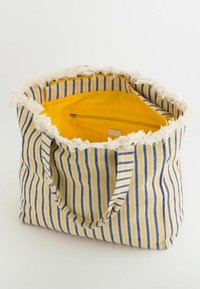 Sac fourre-tout rayé en tissu jaune et bleu avec une bordure en franges. L'intérieur présente une doublure jaune vif et une poche zippée.