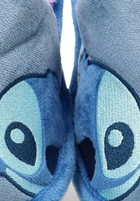 Zapatillas de casa de felpa azul con forma de un personaje, que cuentan con una textura suave, grandes ojos bordados y acentos en tonos de azul más oscuros.