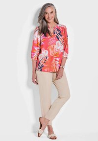 Blusa floreale in rosa, bianco e blu navy con scollo a V e maniche 3/4, abbinata a pantaloni beige e sandali bianchi a scivolo. Tessuto morbido.