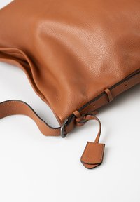 Borsa a spalla in pelle marrone testurizzata con design piatto, tracolla regolabile, cuciture nere e un piccolo etichetta attaccata alla tracolla.
