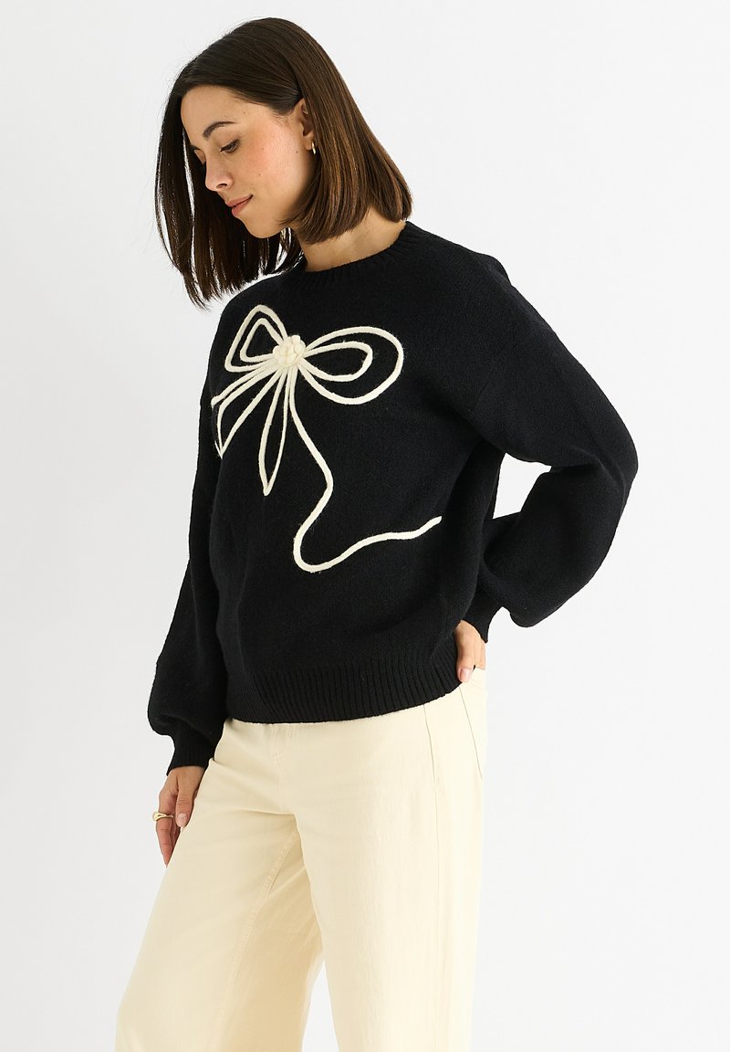 Maglione nero a maglia con un grande motivo a nastro bianco sulla parte anteriore. Il maglione ha una vestibilità morbida e polsini e orlo a coste.