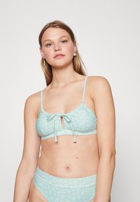Top de bikini azul claro com um design texturizado e franzido, e um fecho frontal com laço; parte de baixo de cintura alta coordenada com tecido texturizado semelhante.