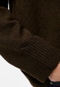 Brown wool sweater detail showcasing a soft texture, ribbed cuffs, and a slightly chunky knit design. Close-up focuses on material quality.