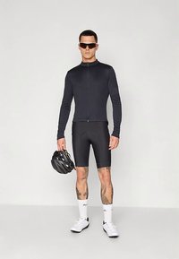 Vyrų dviratininkas vilki juodą ilgą rankovę maikutę, paminkštintas kelnes, baltas kojines, baltus dviratininkų batus ir akinius nuo saulės, laiko juodą šalmą.